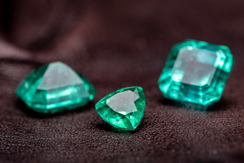 three emerald gemstones sitting on dark brown leather
