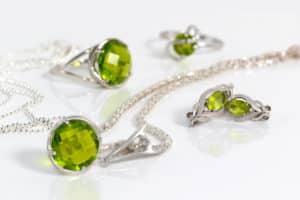 Close-up silver earrings and pendant with peridot on background chain and rings on white acrylic desk.