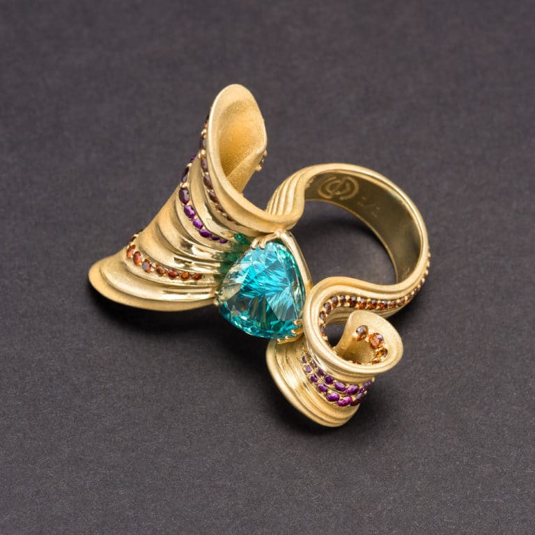 Blue Ziron ring is titled "Ribbon Candy" and is from the genius mind of Erik Stewart. Eric used purple and orange diamonds to accent the deep but perfect sandblast finish of the 18K gold. Whimsical and yet, very serious art.
