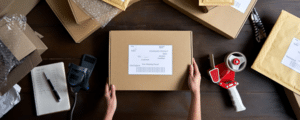 A person packing and labeling a shipping box at a desk with packing supplies.