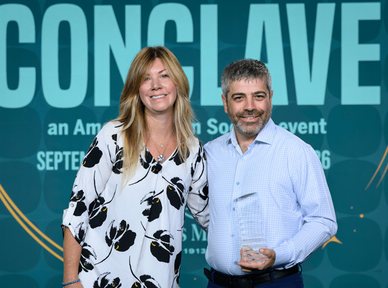 Sallie Morton posing with an award recipient holding a glass trophy in front of a Conclave 2026 backdrop.