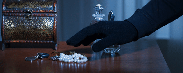 A gloved hand reaching for a pearl bracelet and keys beside an open jewelry box on a table.