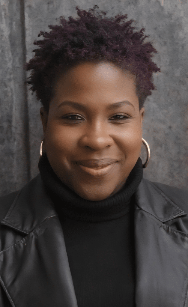 Portrait of Suzanne Dunn smiling in a black leather jacket and hoop earrings.